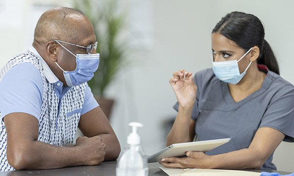A Nurse talking to a BAME patient, both wearing face masks