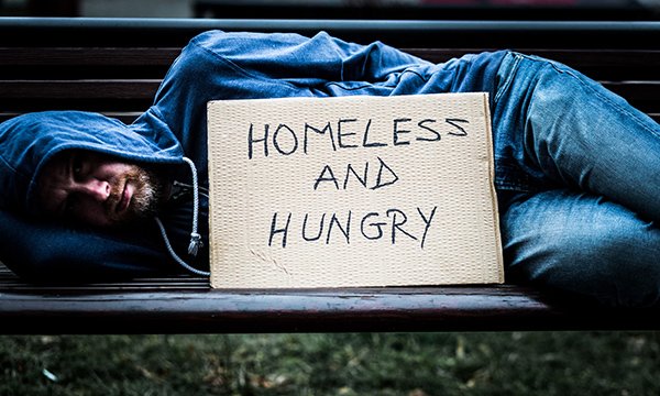 A man sleeping on a bench with a sign saying ‘Homeless and Hungry’: people experiencing homelessness have very poor health outcomes
