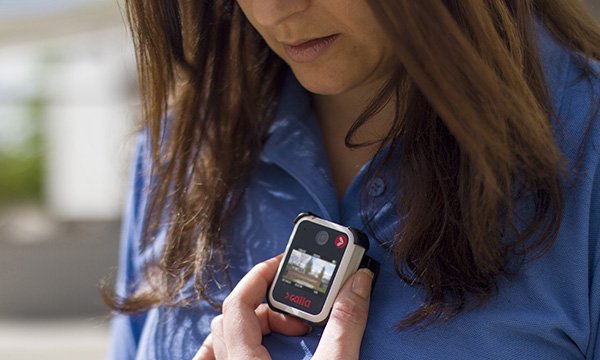 A nurse touches a body-worn camera that is attached to the front of her blouse