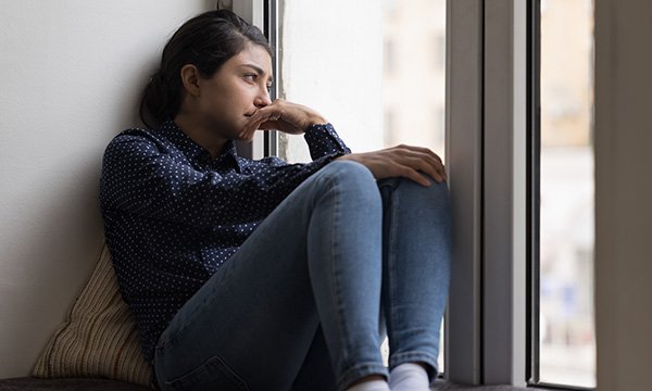 A woman sits on a window sill looking outside, appearing depsondent. Some nurses who face fitness to practise proceedings say they experience depression, suicidal thoughts and professional alienation as a result