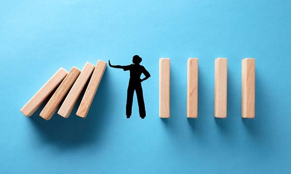 Illustration showing a figure in black on a blue background standing in the middle of a row of giant dominoes, with one arm outstretched to prevent the dominoes to the left falling, suggesting falls prevention