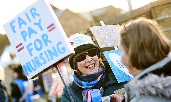 Nurse smiles on picket line during RCN pay strike in England’s NHS, holding banner calling for ‘fair pay for nursing’