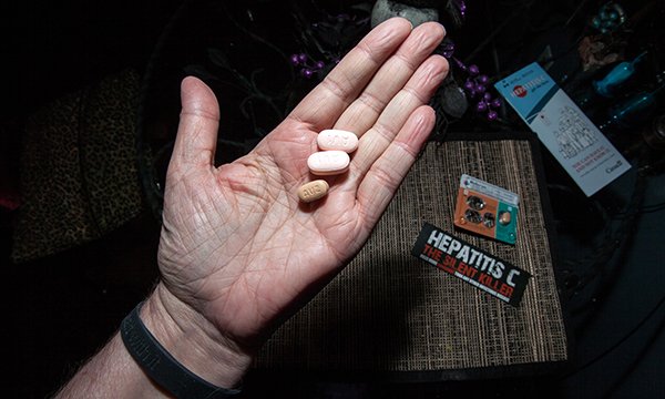Hand holding pills with hepatitis C test on table in front of it